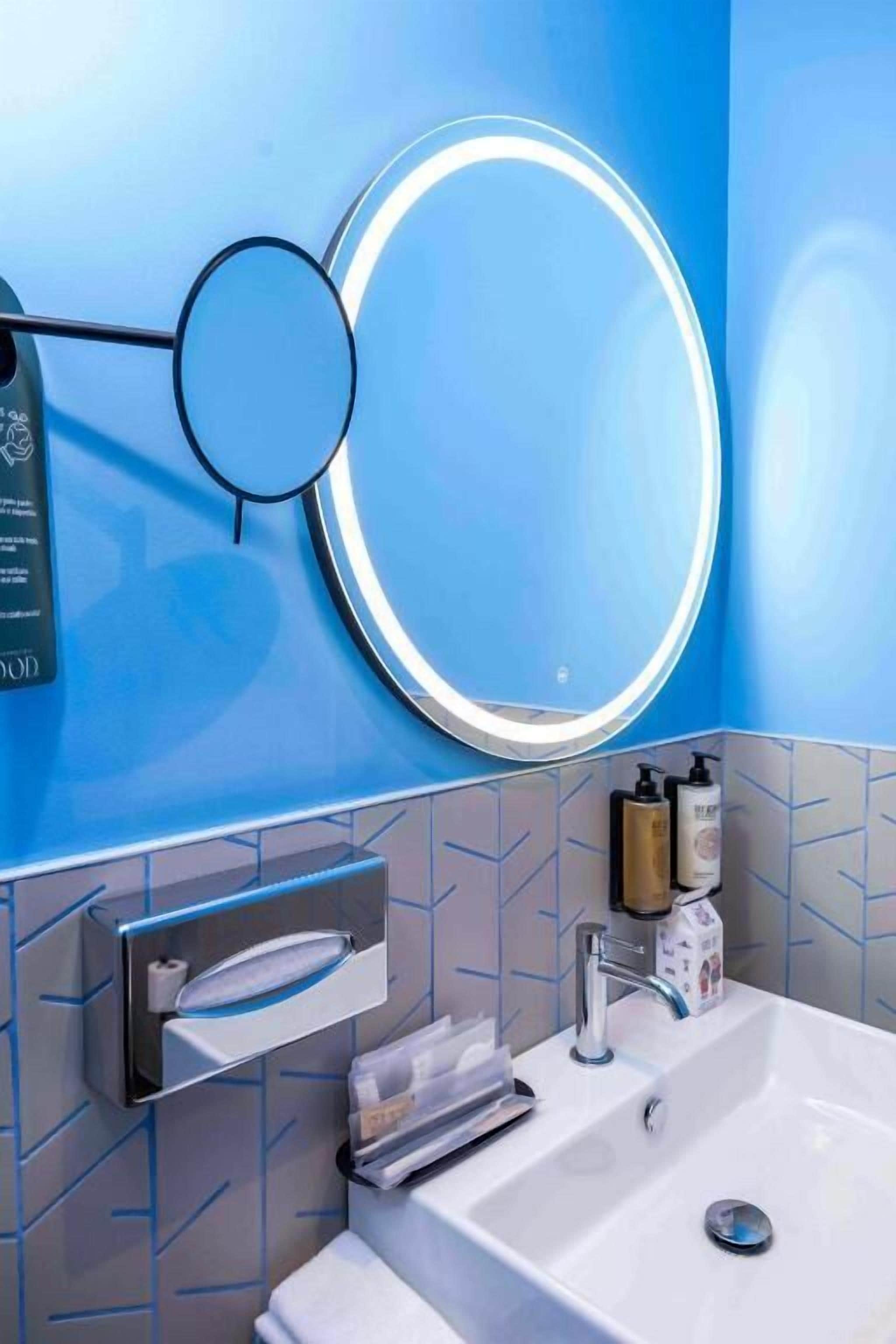 Un baño con un espejo grande, un lavamanos y un perchero para toallas.