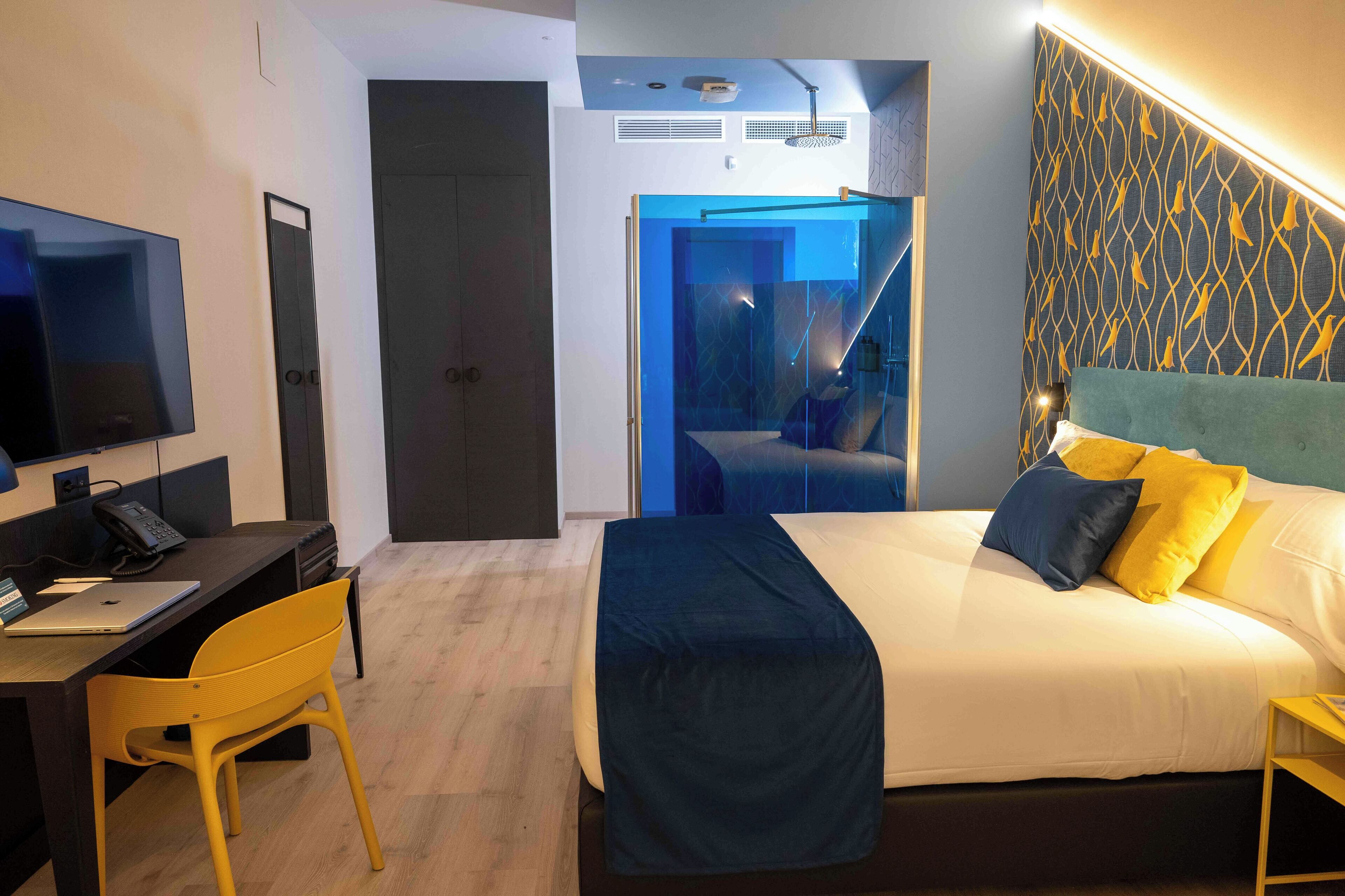 A modern hotel room with a bed, desk, chair, and a TV.
