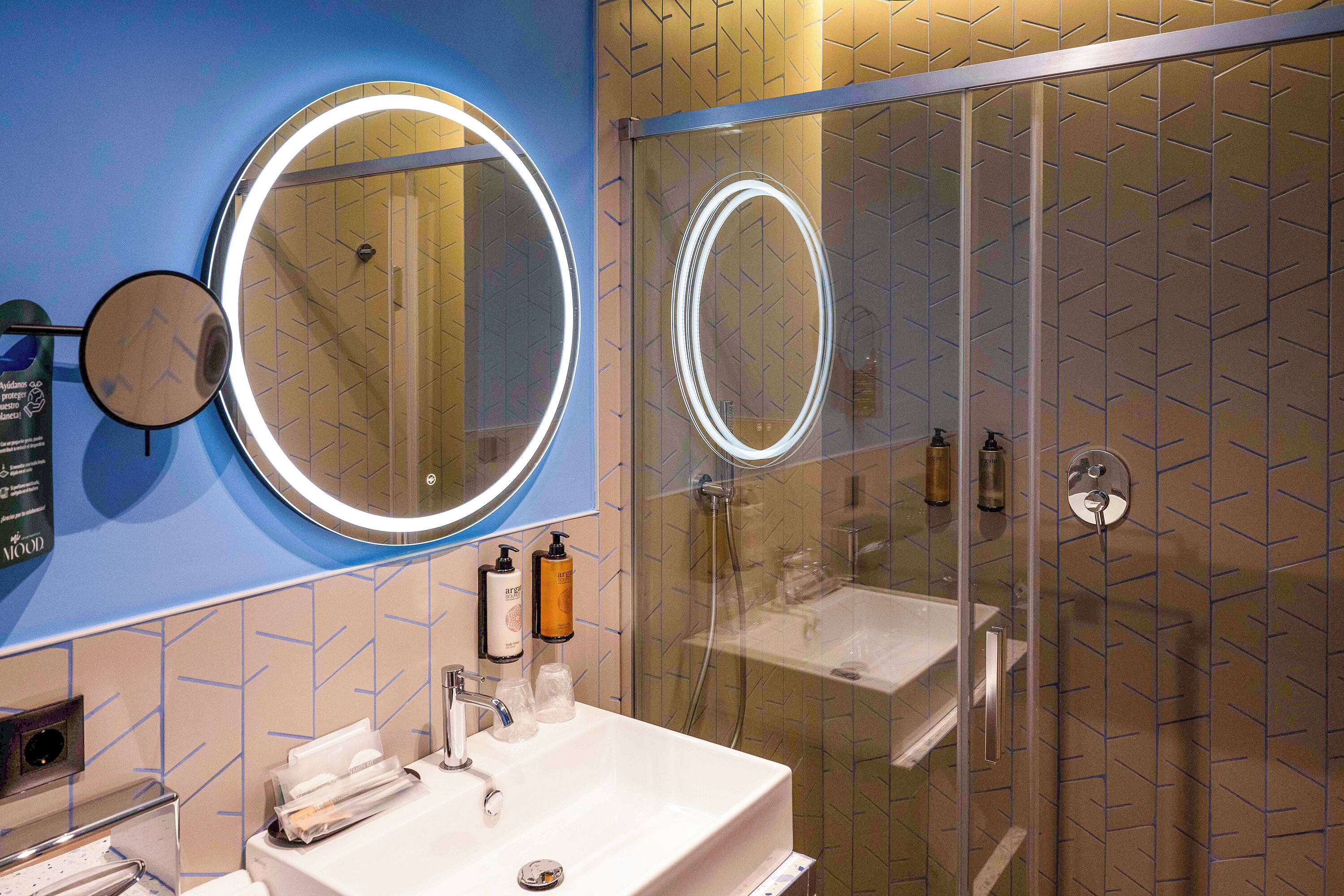 Un baño moderno con ducha de vidrio, un lavamanos blanco con espejo y artículos de aseo en la encimera.