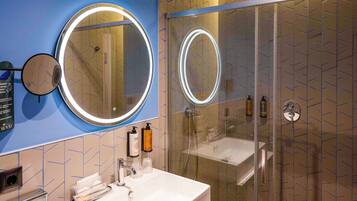 Un baño moderno con ducha de vidrio, un lavamanos blanco con espejo y artículos de aseo en la encimera.