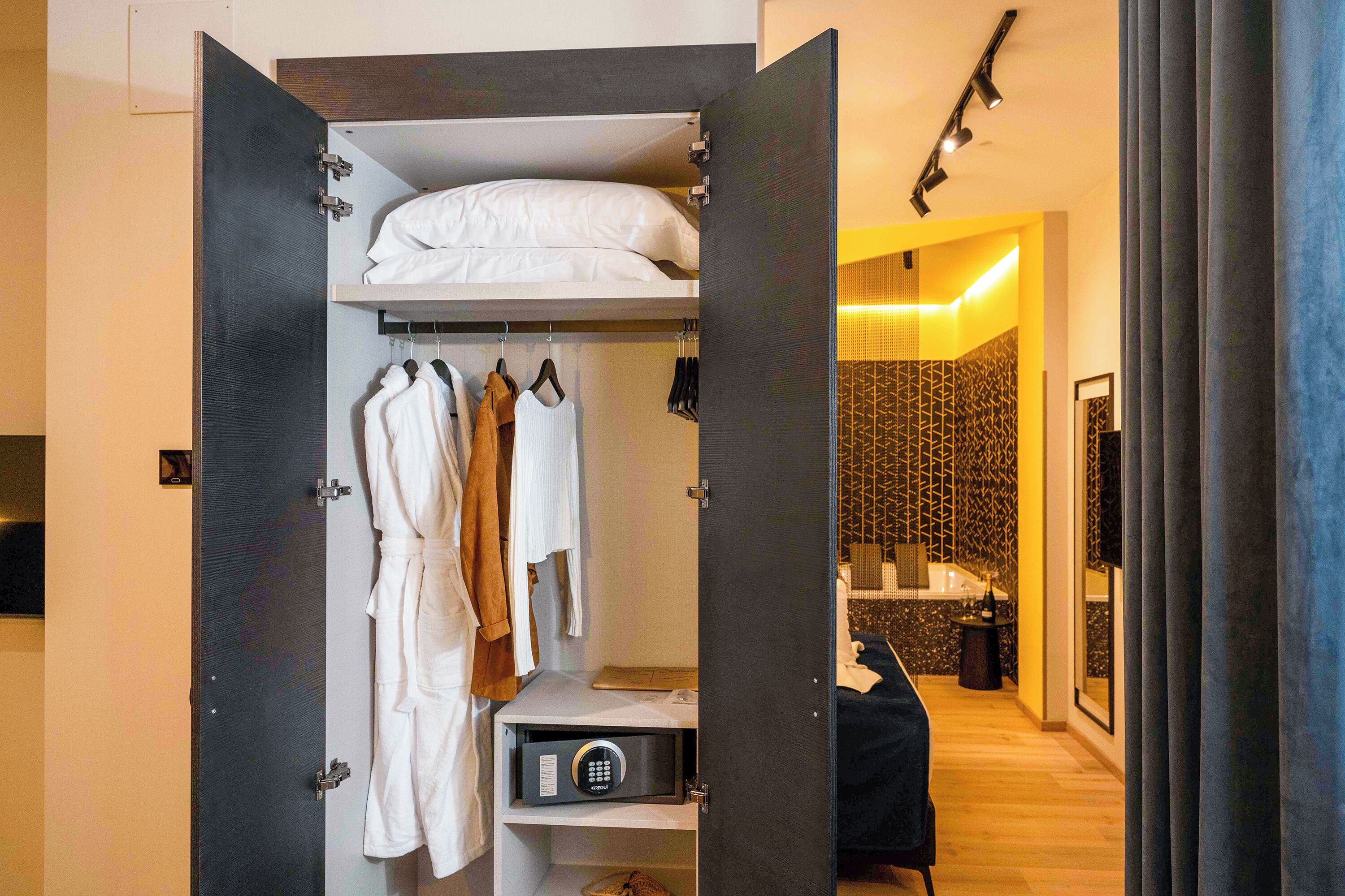 Hotelkamer met inloopkast, met daarin een bed, opbergruimte voor jassen en een kluis.