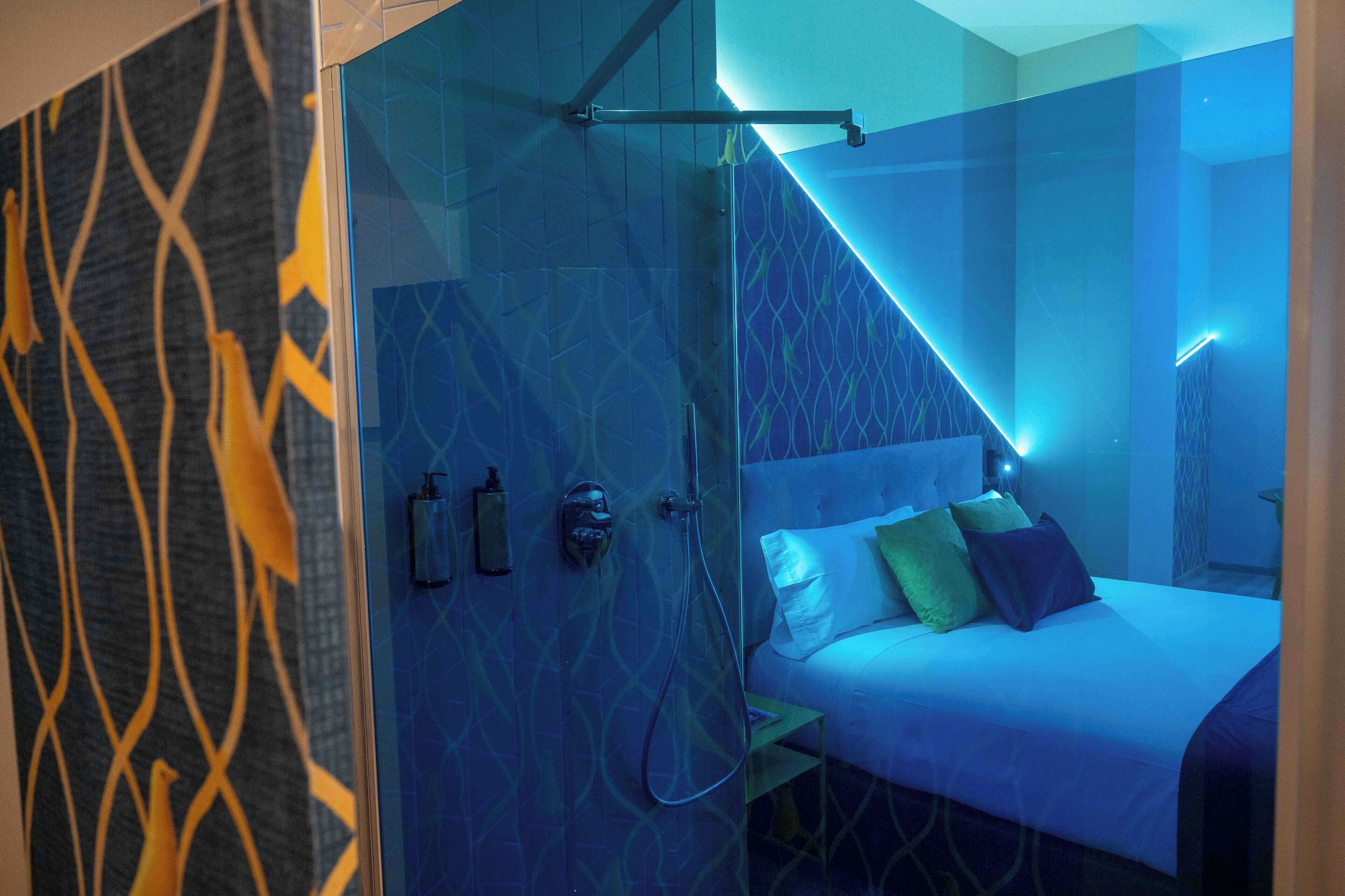 Una habitación de hotel moderna con cabina de ducha de vidrio, una cama con muchas almohadas y una mesita de noche.