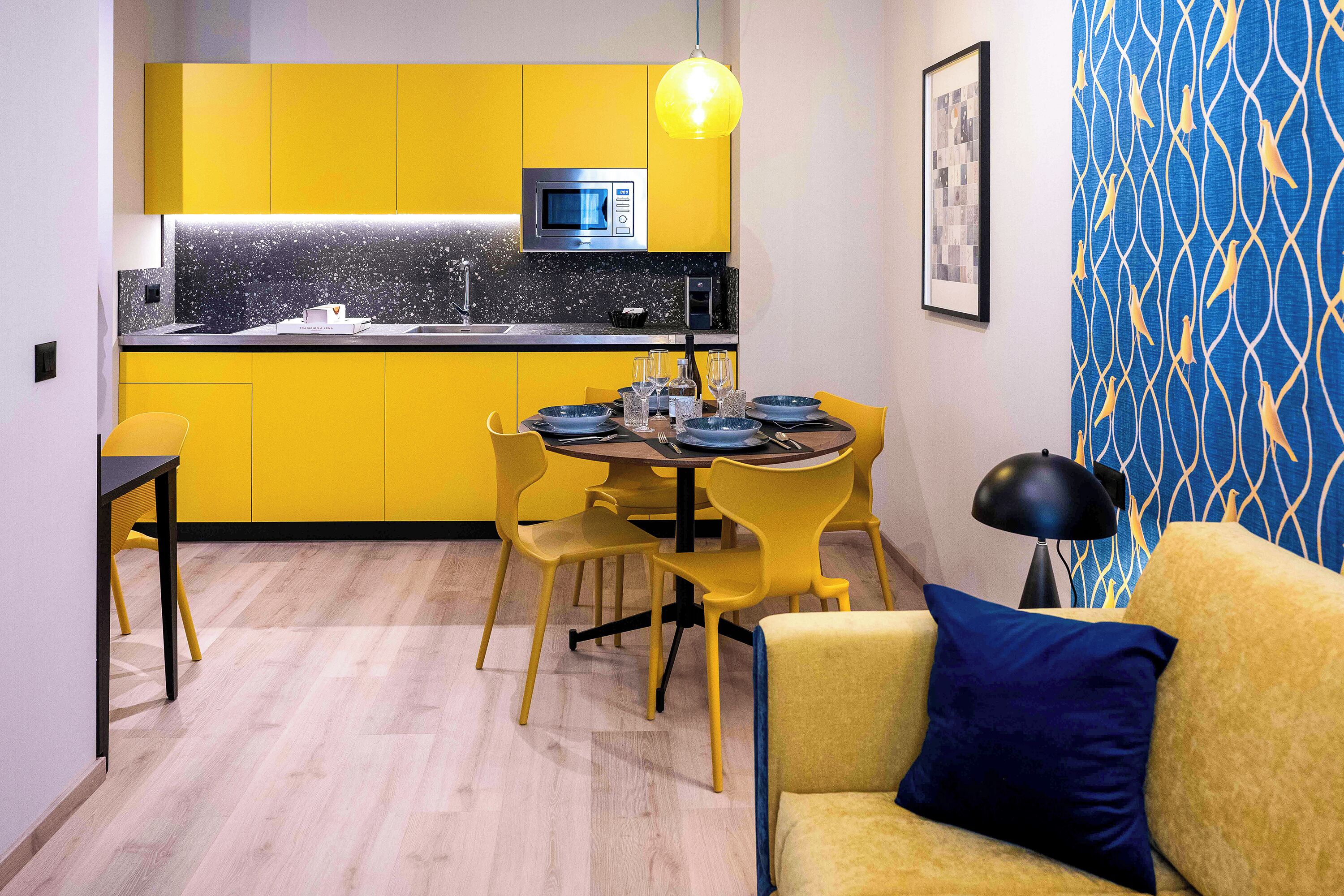 A compact kitchen with yellow cabinets, a microwave, and a dining area with yellow chairs and a table set for four.
