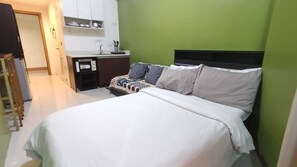 A hotel room with a bed, a kitchenette, and a green wall.