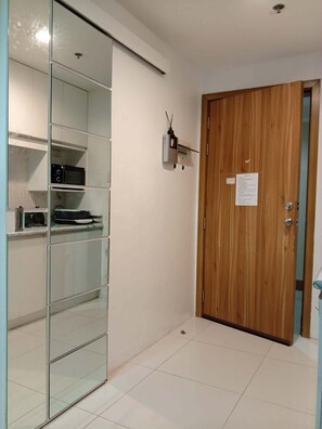 Une pièce avec une porte en bois, une petite étagère sur laquelle se trouve un micro-ondes, et une cloison en verre.