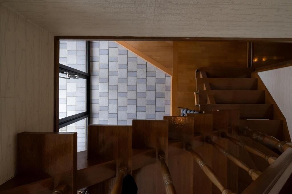 A wooden staircase with a view of a tiled wall and a window.