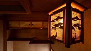 A traditional Japanese interior with a wooden ceiling and a lantern with a silhouette of a mountain and trees. - Nakamachi House (Biei)