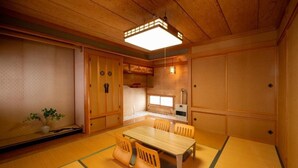 A traditional Japanese-style room with tatami flooring, a wooden dining table with chairs, a small kitchen area, and sliding doors. - Nakamachi House (Biei)