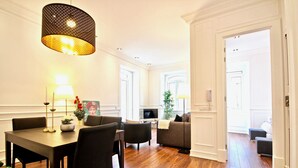 Ein modernes Wohnzimmer mit Essbereich, mit Holzboden, einer Couch, einem Fernseher und einer großen Hängelampe.
