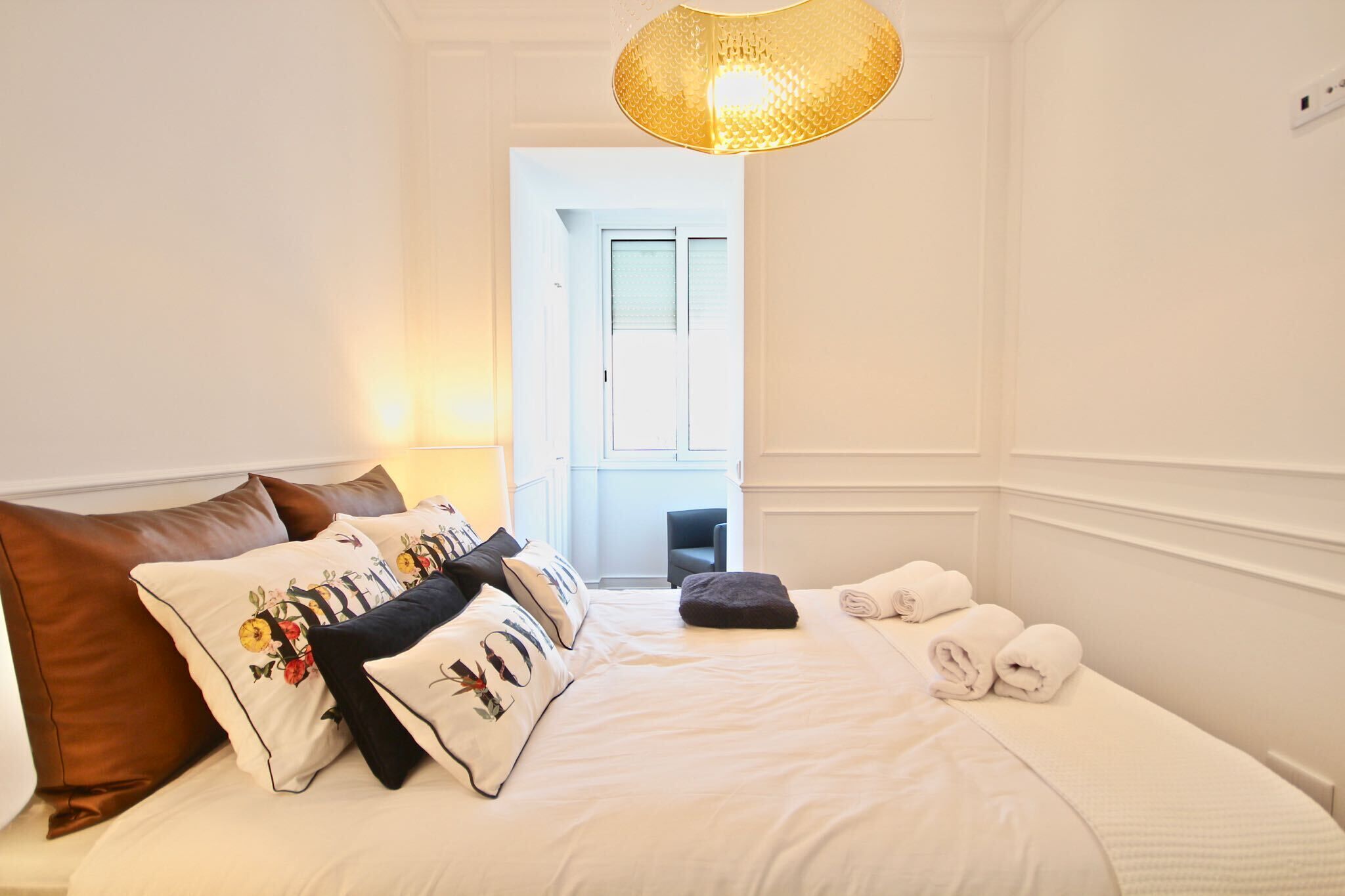 Habitación de hotel con una cama bien hecha, una zona de estar con una silla y vistas al exterior a través de una puerta.