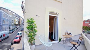 Ein Balkon mit weißem Stuhl, kleinem Tisch und einem Blumentopf.