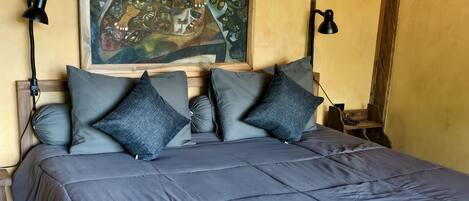 A bedroom with a large bed, wooden headboard, a painting on the wall, and a sloped ceiling.