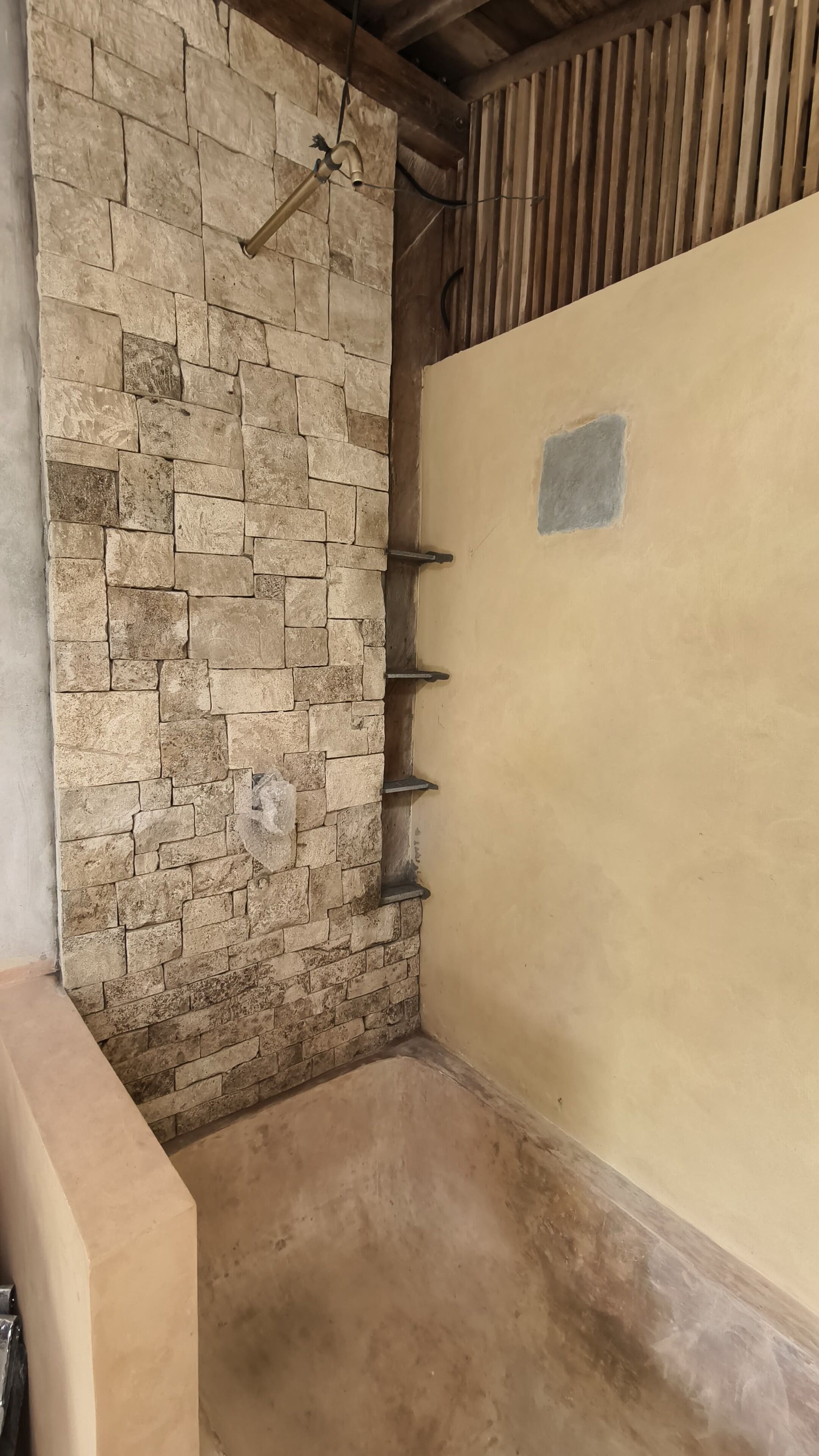 Habitación en esquina con pared de piedra, techo de madera y pared color beige con un ventanal pequeño.