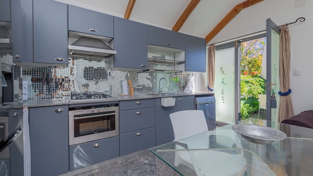 Une cuisine moderne avec des meubles gris, une table à manger en verre et une vue sur le jardin grâce à une porte-fenêtre coulissante.
