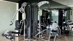 A modern gym with various exercise machines, a wooden floor, and a large mirror on the wall.