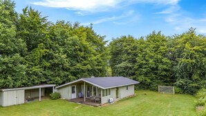 Ein eingeschossiges Gebäude mit einer Veranda, einer kleinen Terrasse und einem überdachten Sitzbereich im Freien.