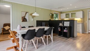 Eine moderne Küche mit weißen Schränken, ein Essbereich mit einem weißen Tisch und schwarzen Stühlen sowie ein Holzboden.
