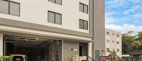 A modern building with a garage entrance, a staircase leading to the entrance, and a clear sky.