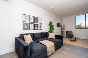 A modern living room with a black sectional sofa, a large green plant, and artwork on the wall. - Stylish Miami 1BR Oasis Near Calle Ocho & Brickell (Miami)