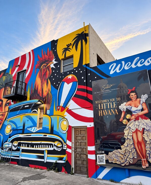 Un edificio con un mural llamativo que muestra un gallo, un coche y una mujer sosteniendo un cóctel.