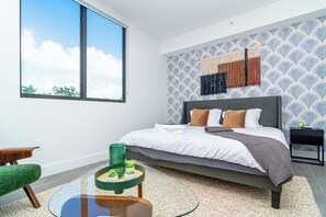 Ein modernes Schlafzimmer mit einem großen Bett, einem grünen Sessel, einem kleinen Tisch mit Pflanzen und einer Wand mit Muster.