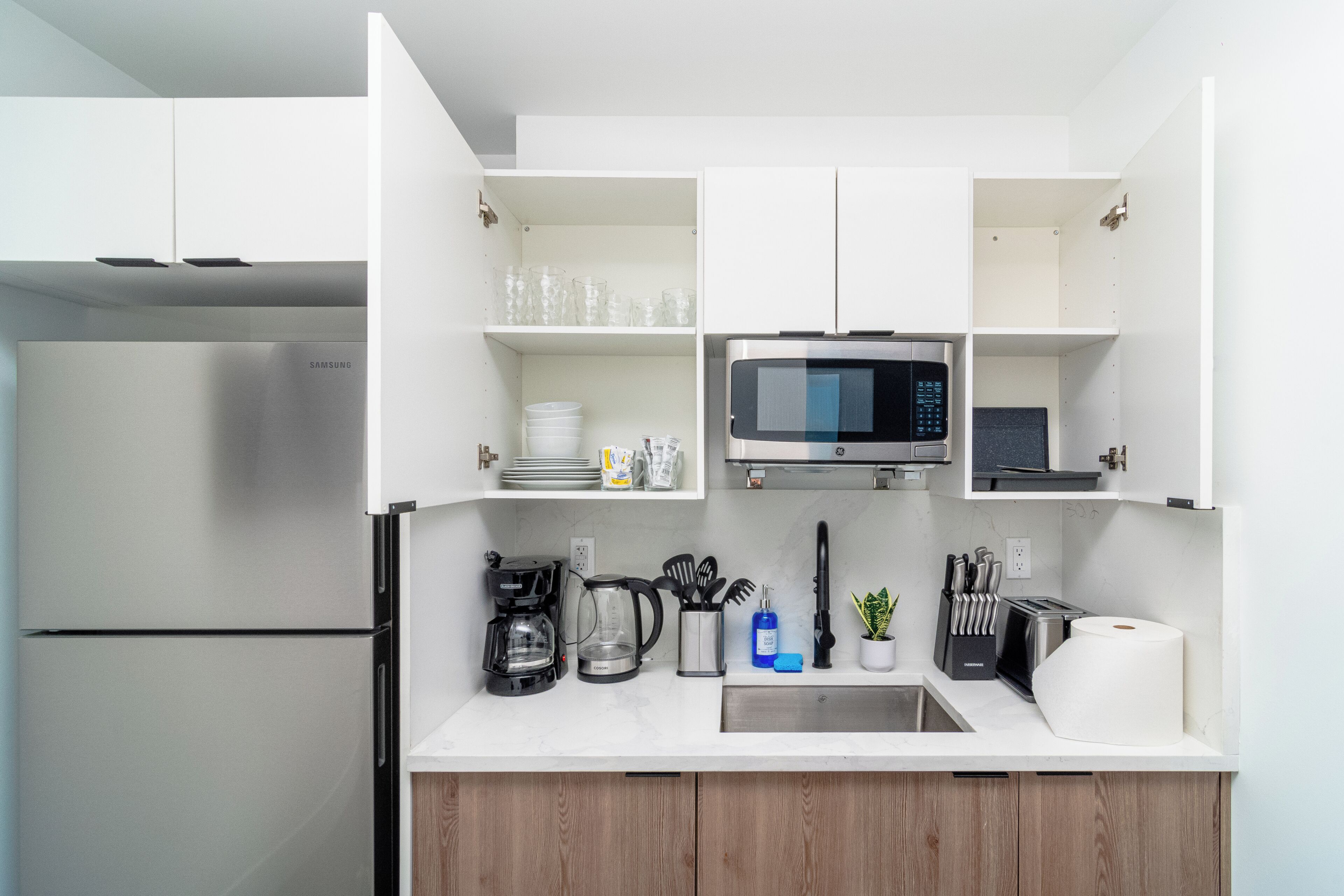 Une cuisine moderne avec des meubles blancs, un réfrigérateur en acier inoxydable, un four à micro-ondes et une machine à café.