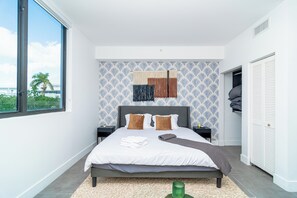 A modern bedroom with a large bed, a view of the outdoors, and a patterned wall.
