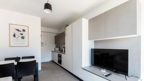 A modern kitchen with a built-in TV, a dining area with a table and chairs, and a framed botanical print on the wall.