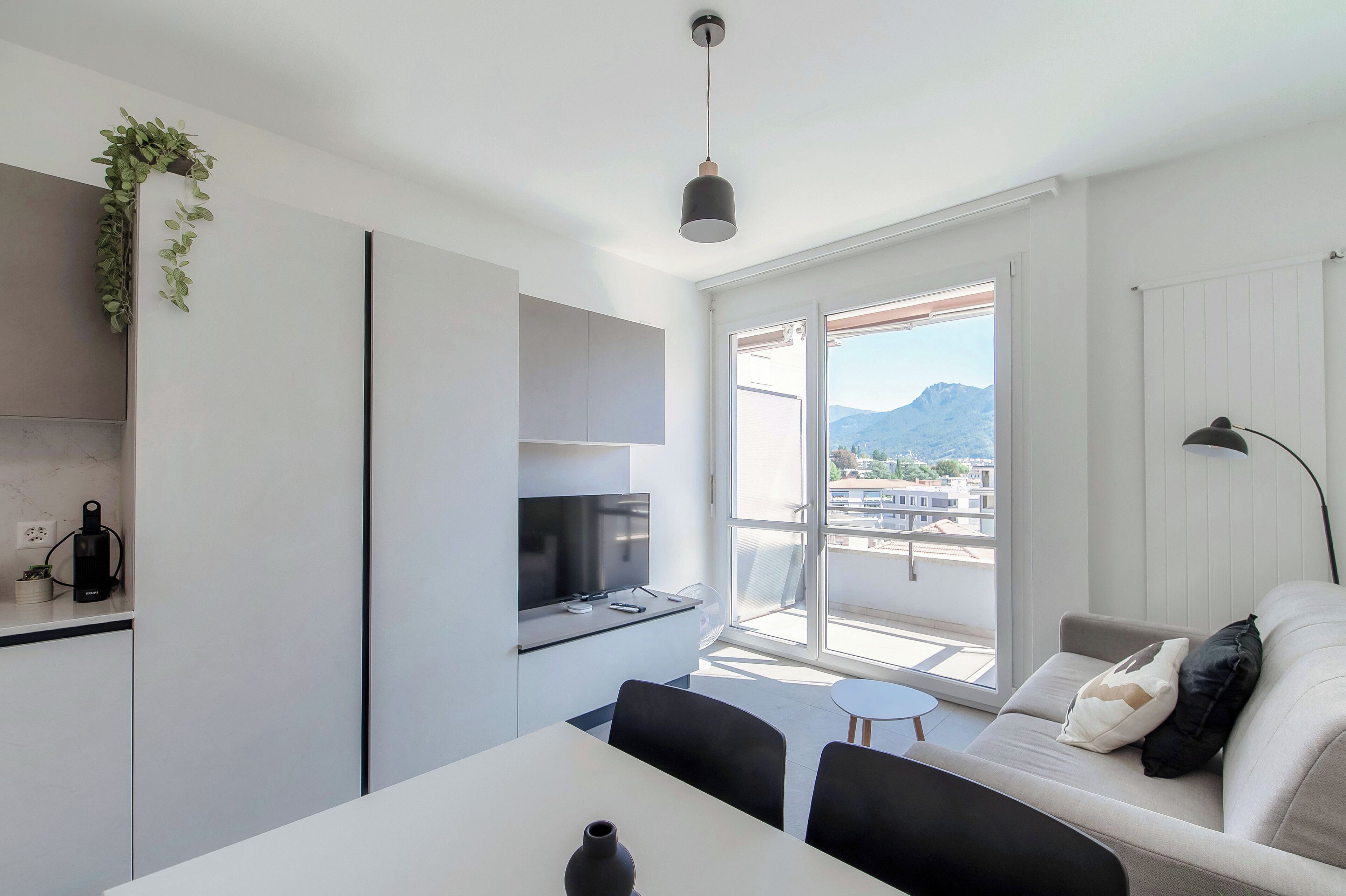 A modern kitchen with a built-in stove, a dining table with chairs, and a large window offering a view of mountains.