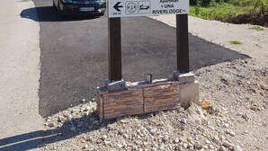 A wooden sign with hiking symbols and a directional arrow indicating a 20m distance to a hostel named 'UNA RIVERLODE'. - Bosnian house next to the Una river, with a view of the old Ostrovica fortress (Kulen Vakuf)