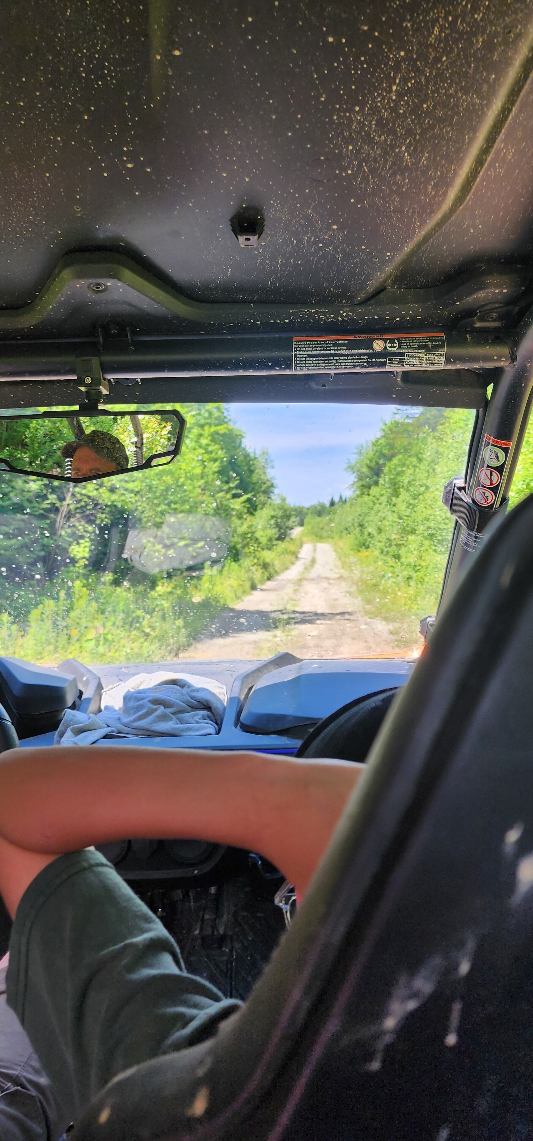 L'intérieur d'un véhicule, avec vue sur un chemin de terre qui traverse une forêt.