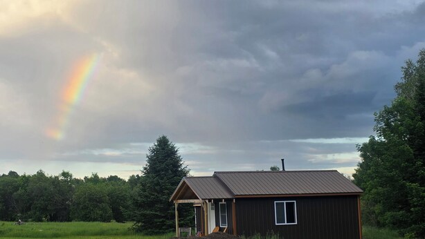 A wooden cabin with a metal roof, surrounded by greenery and a rainbow in the sky. - Charming cabin in Beautiful Patten Maine with WiFi, ATV/Snowmobile trail access (Patten)