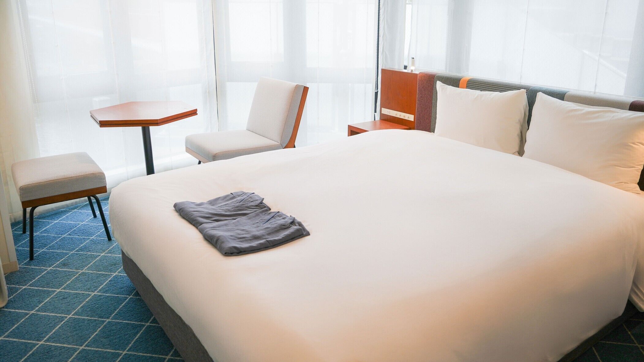 Una habitación de hotel con una cama grande, una mesita, una silla y un banco.