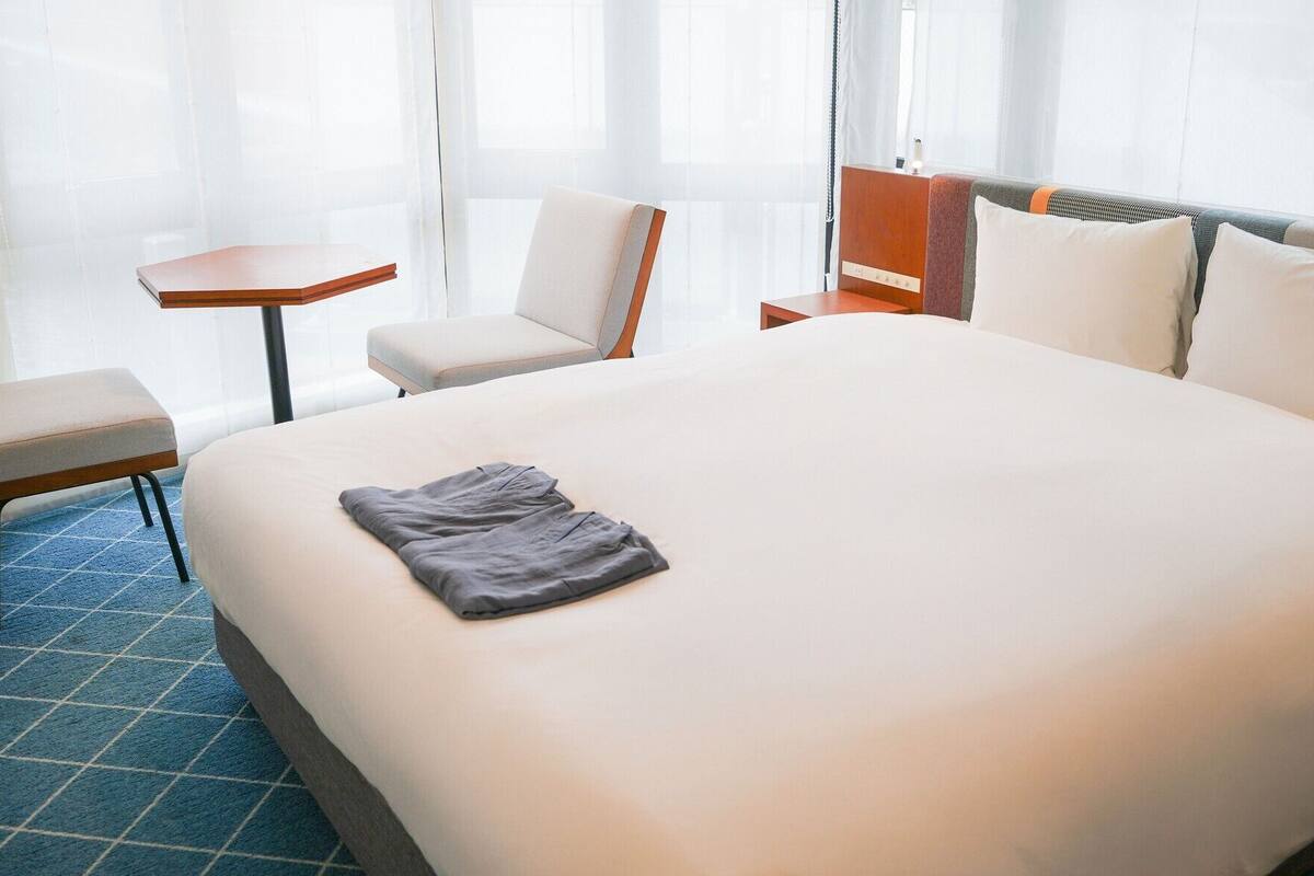 Una habitación de hotel con una cama grande, una mesita, una silla y un banco.