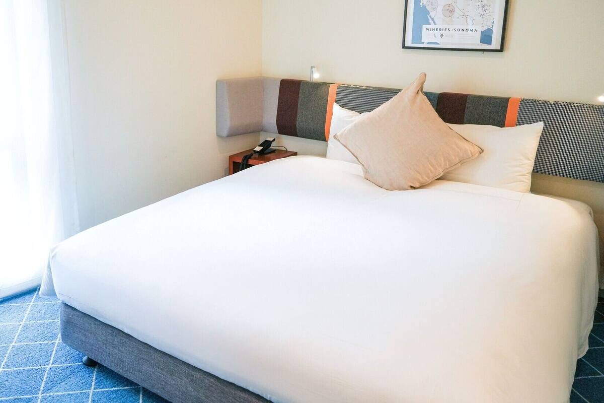Habitación de hotel con una cama grande, una mesita de noche, una lámpara y un mapa enmarcado en la pared.