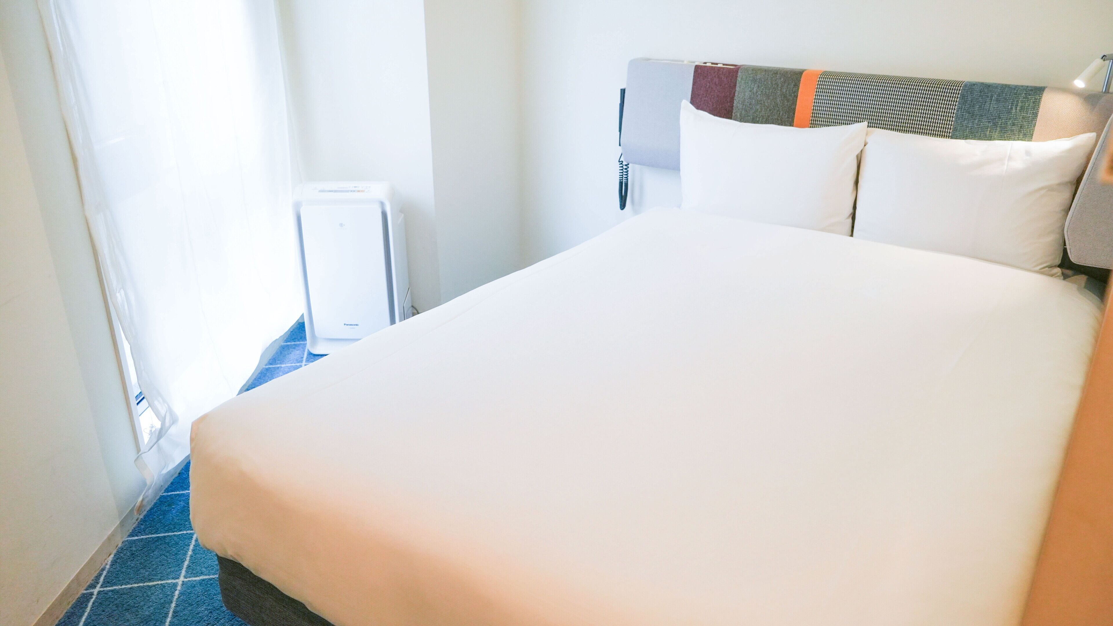 Une chambre d’hôtel avec un grand lit, une table de chevet, une fenêtre avec des rideaux et un radiateur.