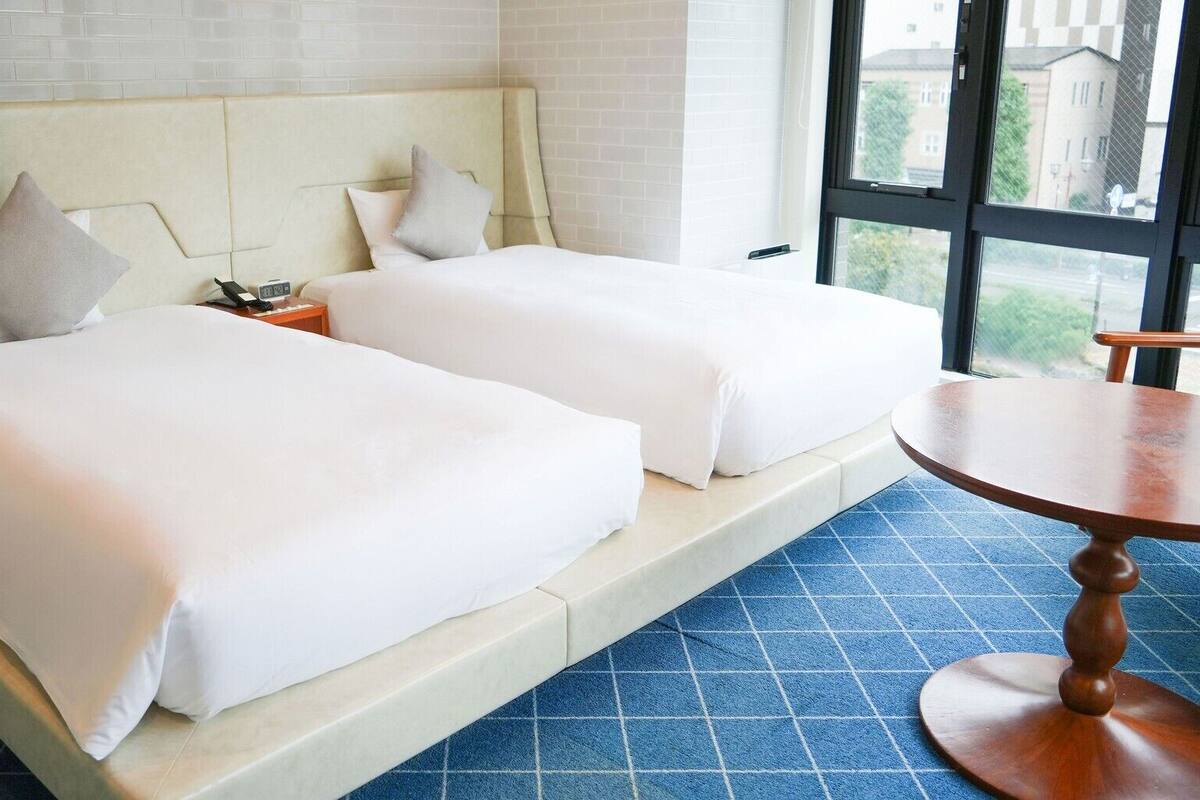 Habitación de hotel con dos camas, una mesita y una ventana con vistas.
