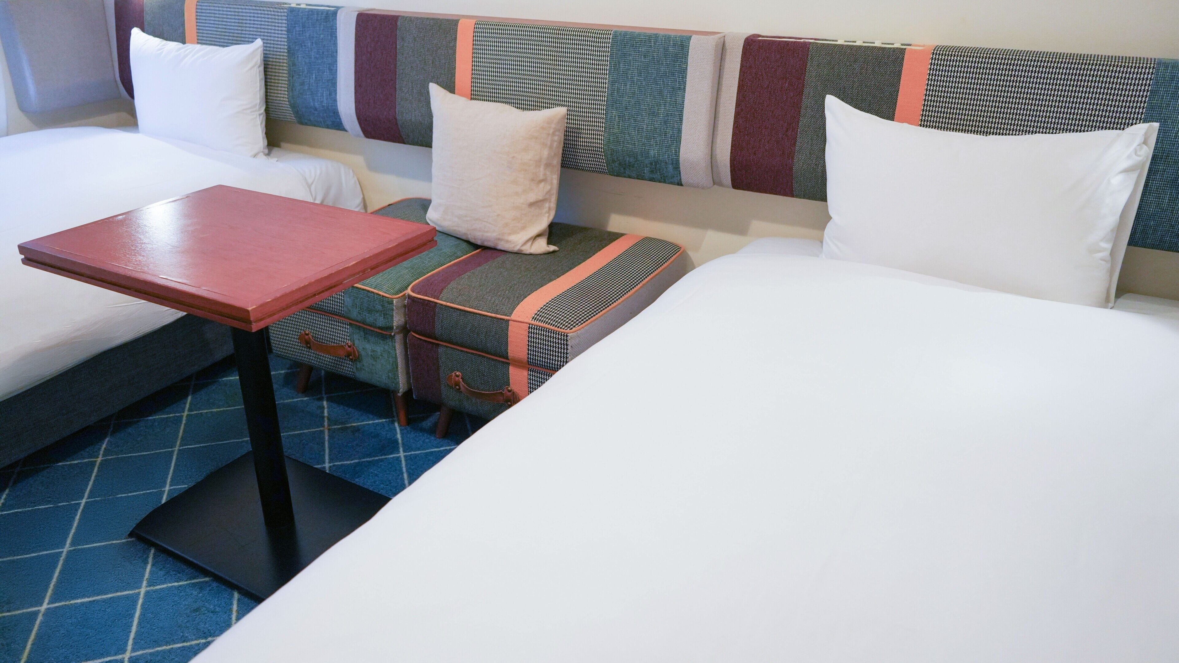 Une chambre d’hôtel avec deux lits, une petite table et un banc avec espace de rangement.
