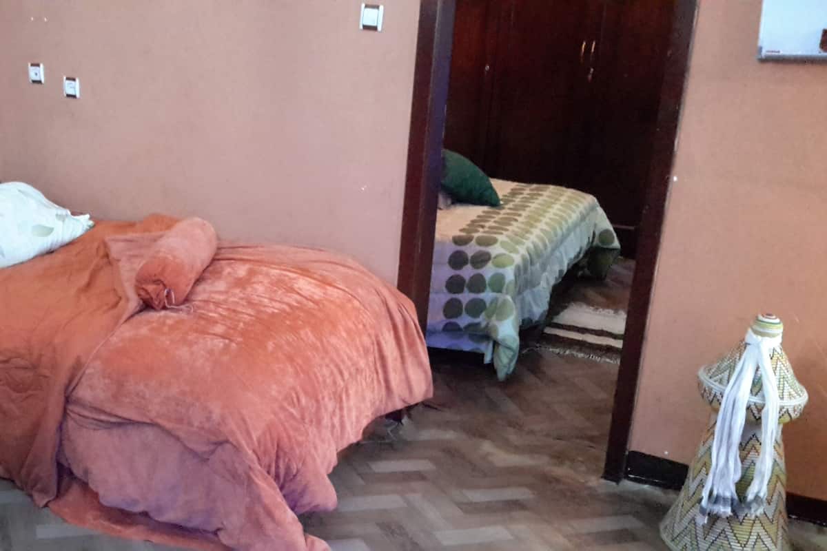 A bedroom with two beds, one with a pink bedspread and the other with a green and white polka dot bedspread.