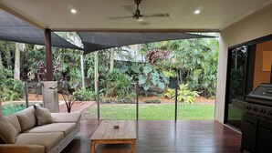 Ein überdachter Patio-Bereich mit Holztisch, Rattan-Sofa und Grill.