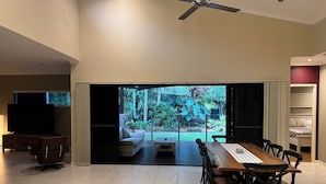 Ein modernes Wohnzimmer mit Essbereich, Fernseher und Blick auf einen Garten durch eine Schiebetür.