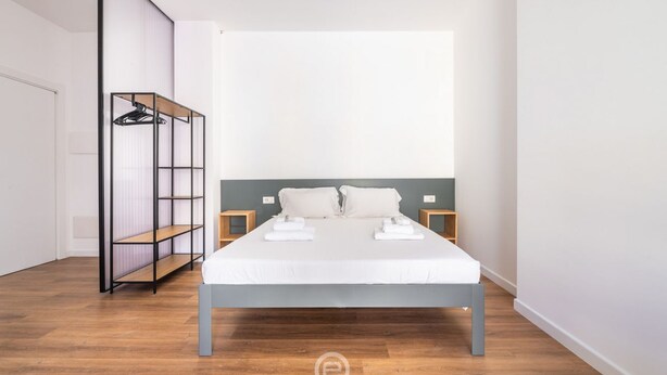A modern bedroom with a large bed, a wardrobe with shelves, and bedside tables.