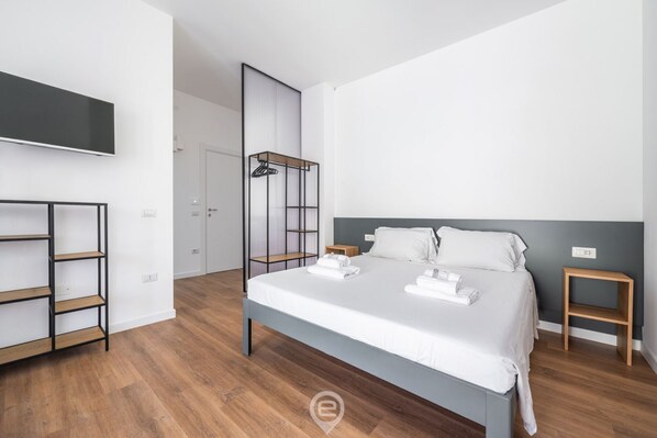Quarto moderno com uma cama grande, TV na parede e piso de madeira.