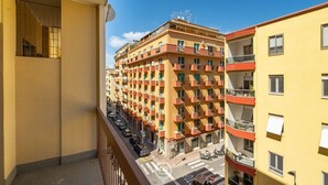 A multi-story residential building with balconies, a street view, and a clear sky.