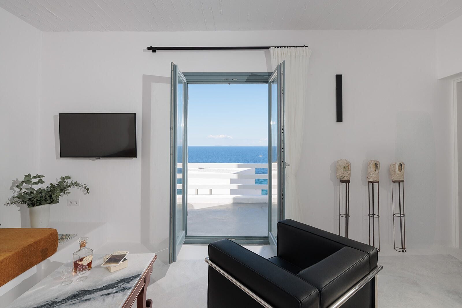A modern room with a glass door leading to a balcony with a view of the sea.
