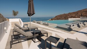 A modern outdoor pool area with lounge chairs and a view of the sea. - Kana Hotel (Naxos)