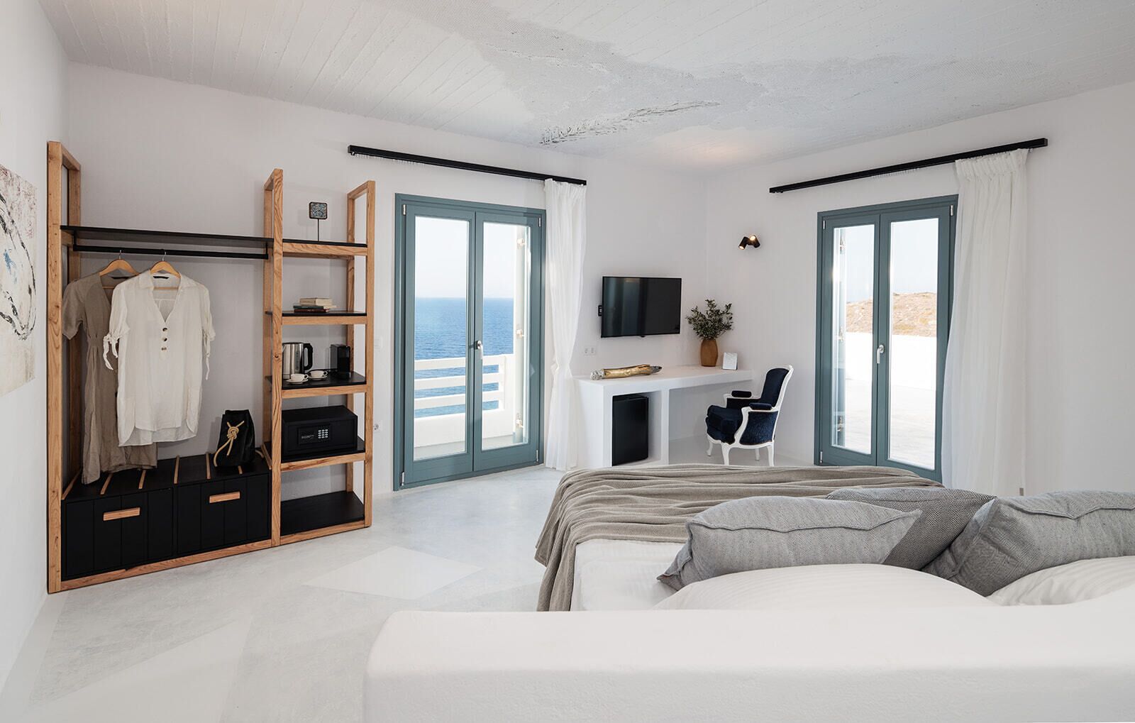 A modern bedroom with a bed, a desk with a TV, a wardrobe, and a balcony with a view of the sea.