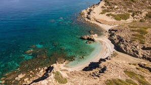 A coastal landscape with clear turquoise waters, rocky terrain, and sparse vegetation. - Kana Hotel (Naxos)