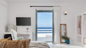 A bedroom with a bed, a TV, a desk, and a view of the sea. - Kana Hotel (Naxos)