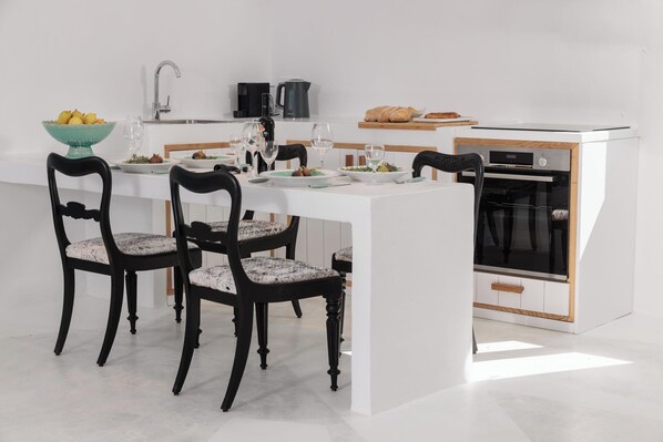 Une cuisine moderne avec un îlot central, des chaises noires, une table blanche et un four encastré.